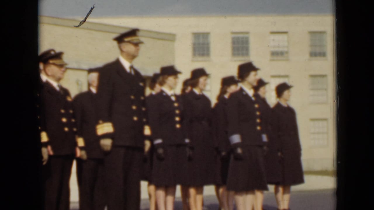 Uniformed officers and women stand in formation beside a light-colored building.