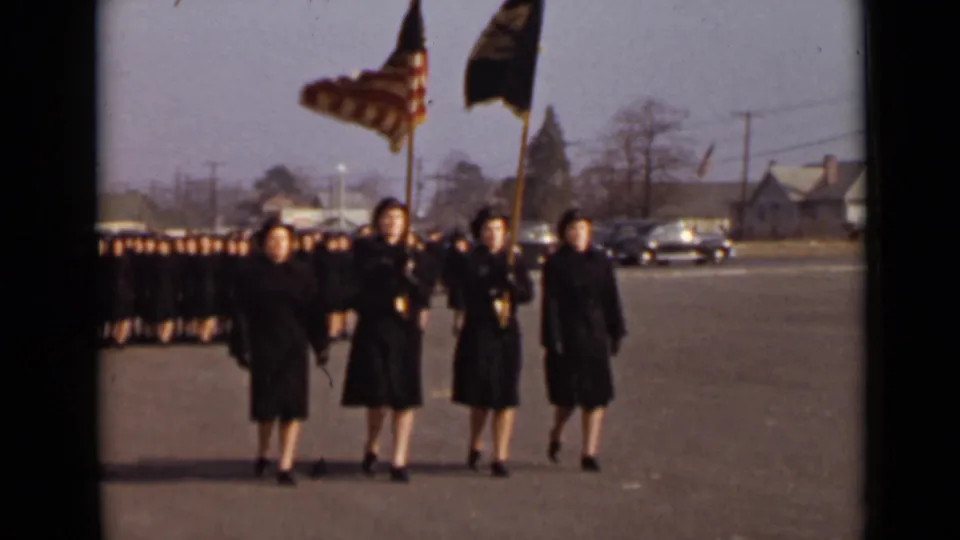 1947 New York frame showing four uniformed women leading a larger formation, with an American flag and dark organizational banner above them.