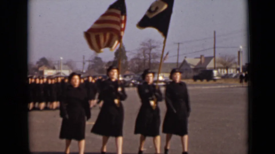 Closer 1947 New York view of uniformed women carrying an American flag and a dark banner while marching before a larger formation.