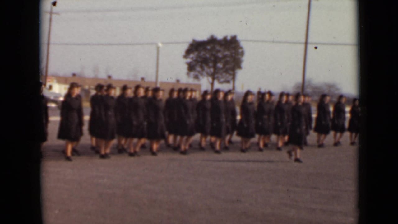 Rows of women in dark matching clothing continue marching past the camera.
