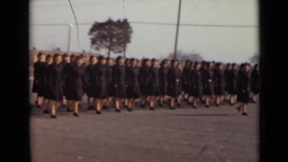 Closer 8mm view of women in matching dark outfits marching together across a paved area in 1947 New York.
