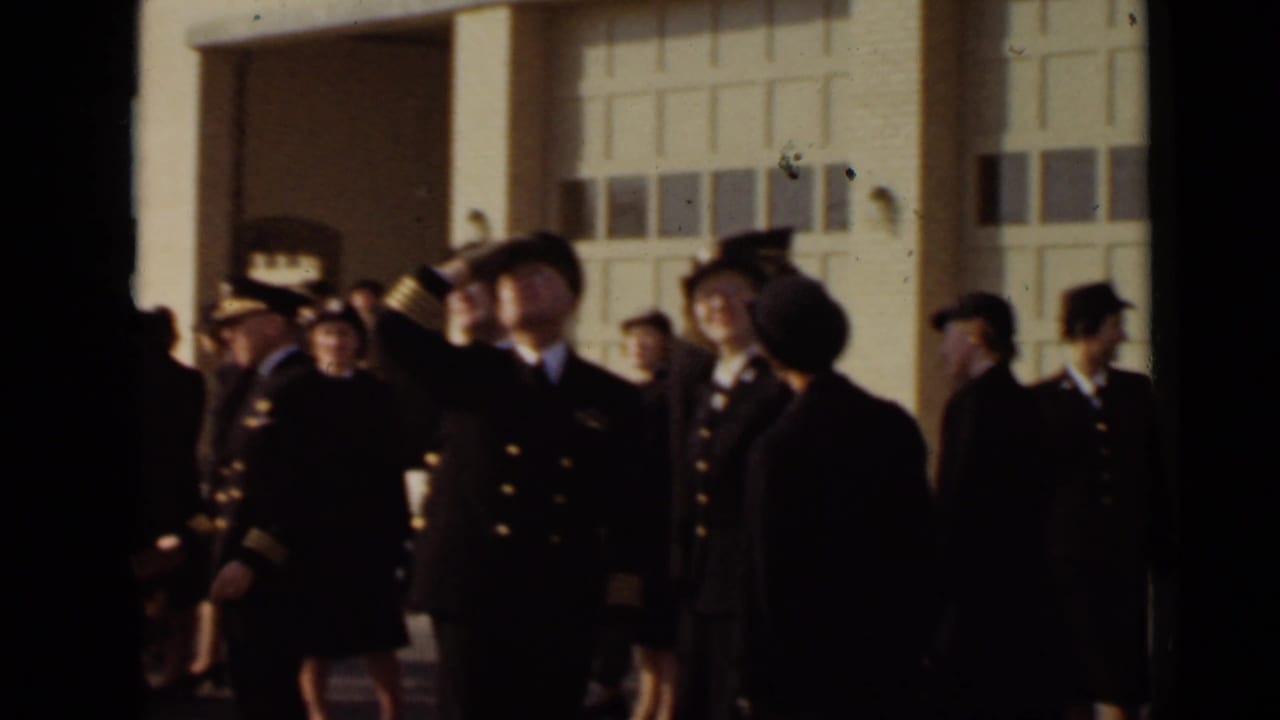 Uniformed officers and women stand outside large paneled doors as one man salutes.