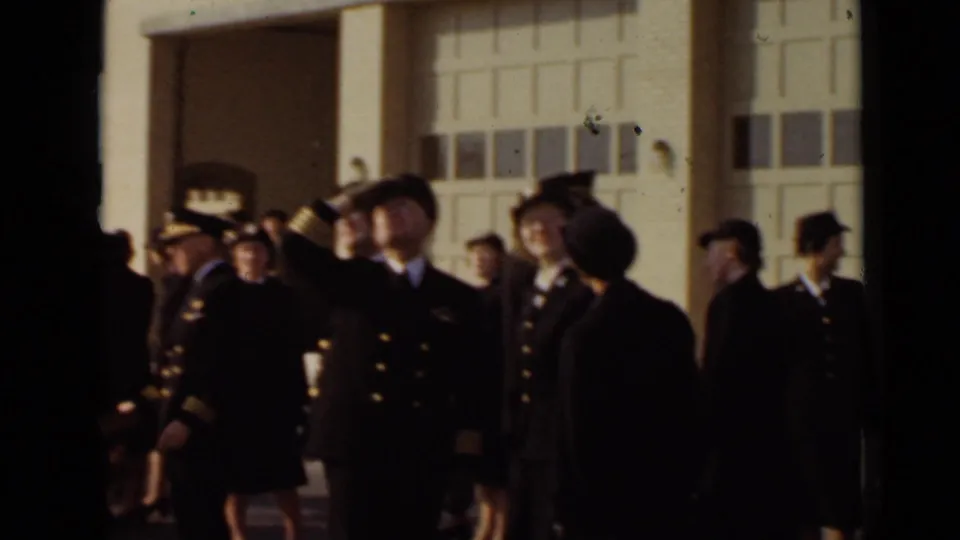 In 1947 New York footage, uniformed officers and women gather outside a brick building while a male officer raises a salute.