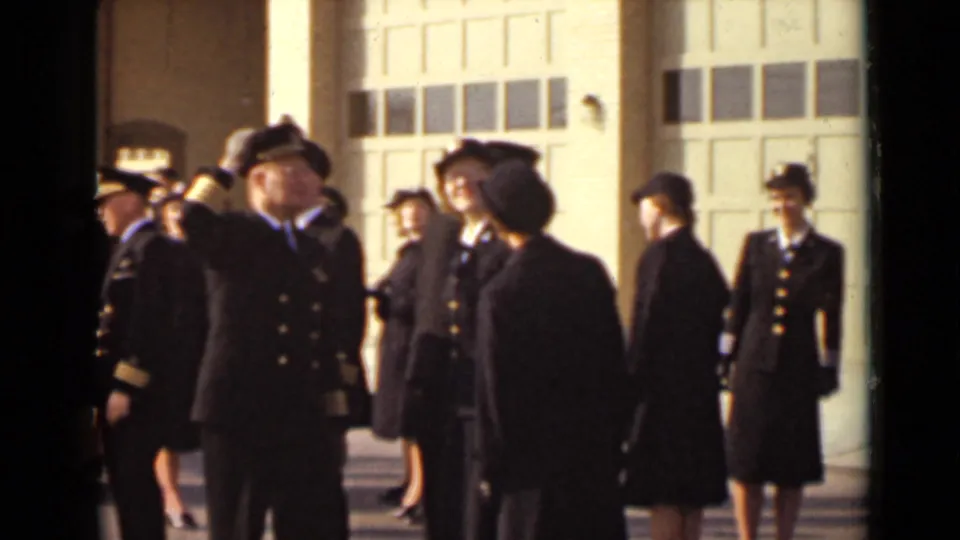 A group of uniformed men and women appears outside a New York building, with one male officer saluting near the center.