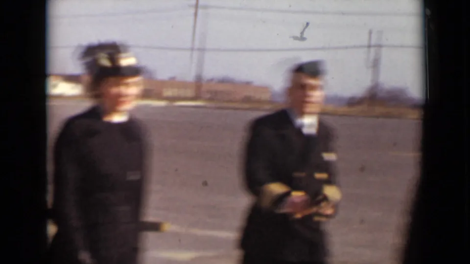 1947 New York home-movie frame showing two women in dark service-style uniforms on a paved parade ground or parking area.