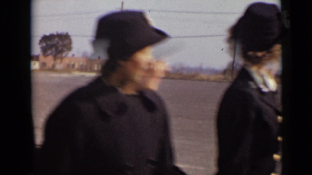 Uniformed women in dark hats and coats appear close to the camera on a paved New York setting in 1947.