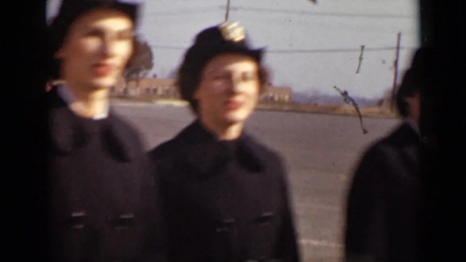 Close 8mm frame of two women in dark uniforms, one smiling toward the camera, in the 1947 New York clip.
