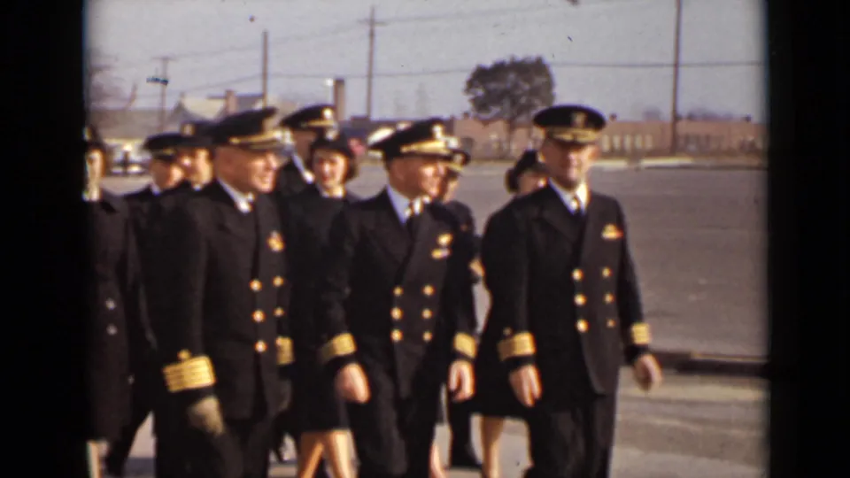 Several male officers in dark naval-style uniforms with gold sleeve trim walk in front of uniformed women in a 1947 New York outdoor scene.