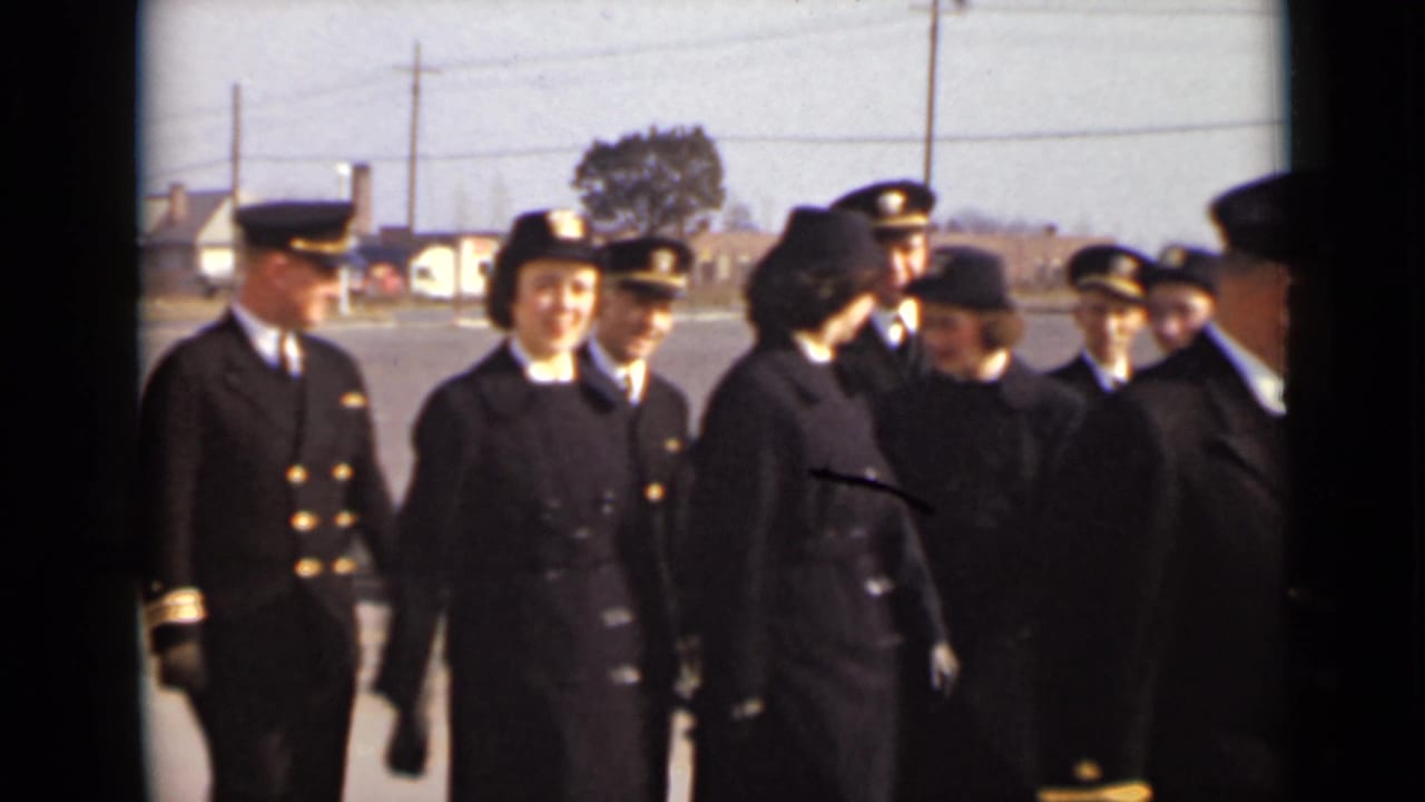 Uniformed men and women walk outdoors across a paved area.