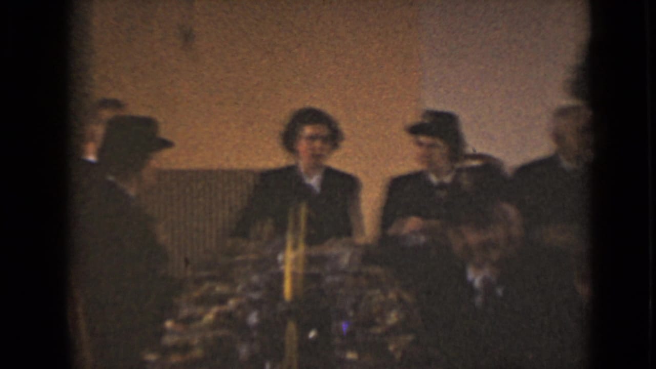 Adults in dark formal clothing sit around a table with candles and flowers.