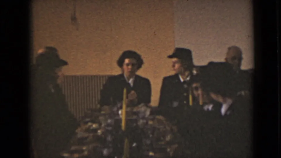 1947 New York indoor meeting scene with adults in formal dress seated beside candles and flowers.