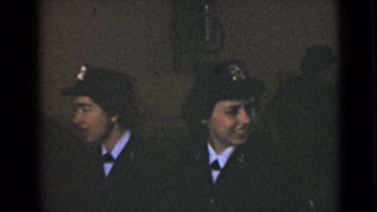Two women in dark uniforms and peaked caps sit in a dim interior.