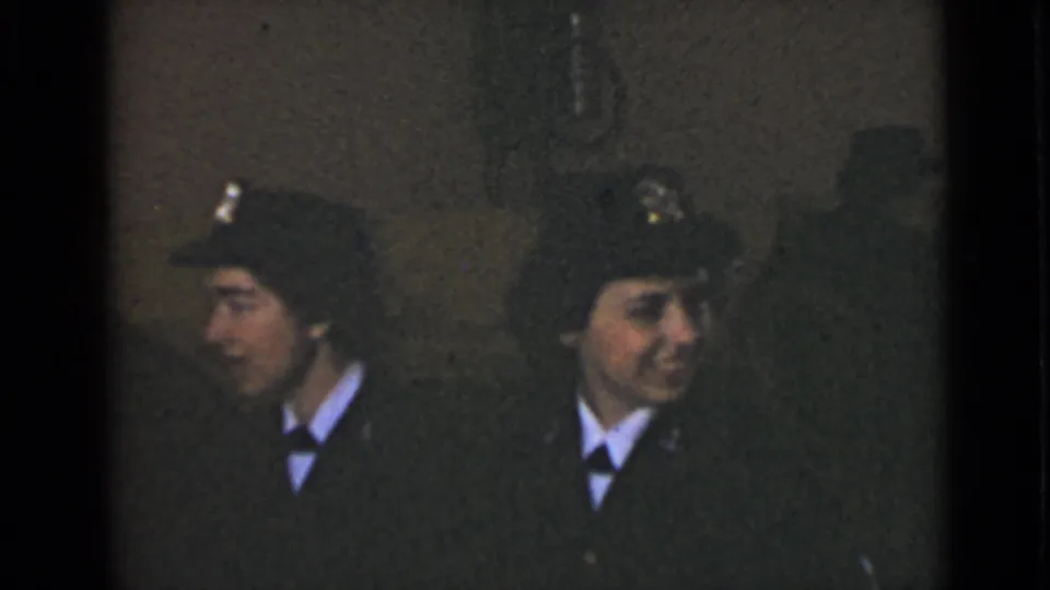 Two uniformed women in dark caps and white collars sit close together in a dim 1947 New York interior.
