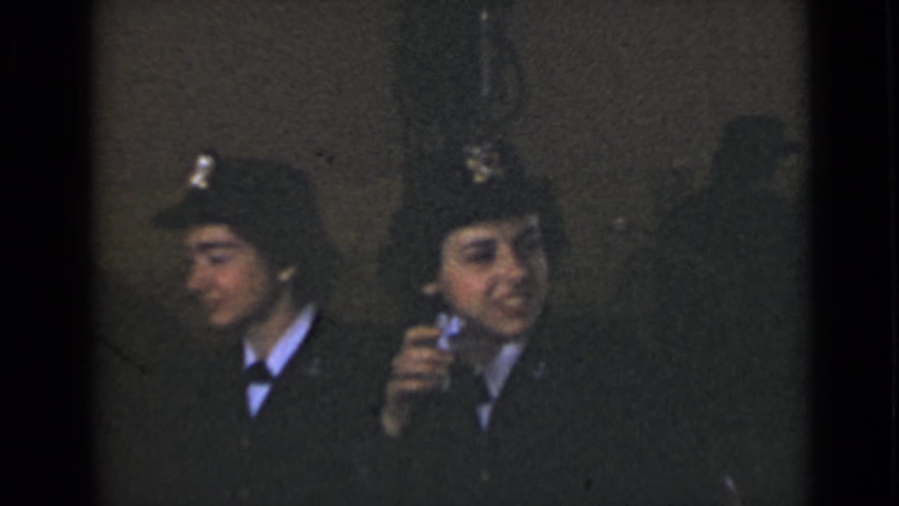 Two uniformed women sit together, one holding an object near her face.