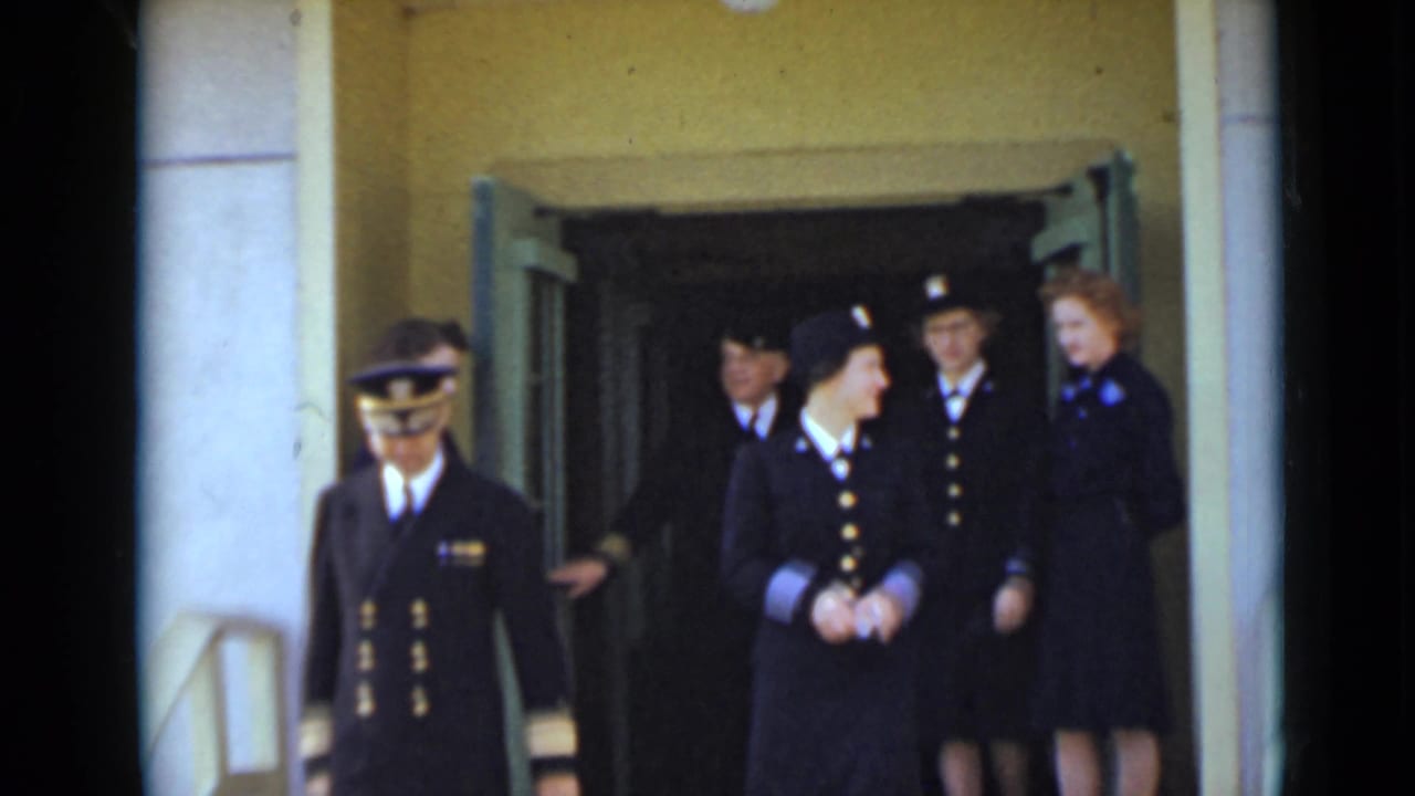 A uniformed man and several women in dark military-style uniforms leave a New York building entrance in 1947 home-movie footage.