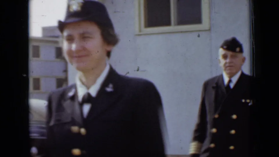 In 1947 New York footage, a woman in a dark uniform and cap passes close to camera while a male officer stands behind her.