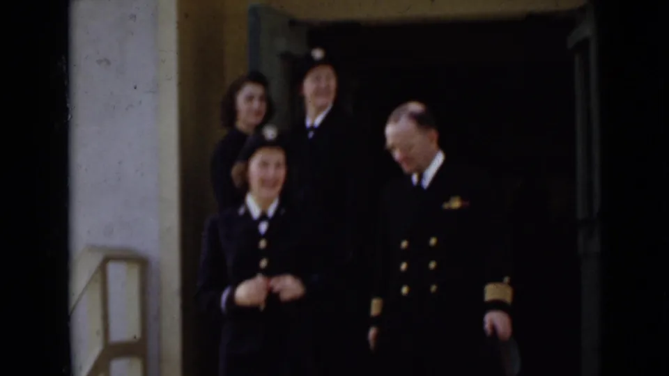 Several uniformed adults gather at a doorway in New York, with a male officer and women in dark service-style clothing visible.