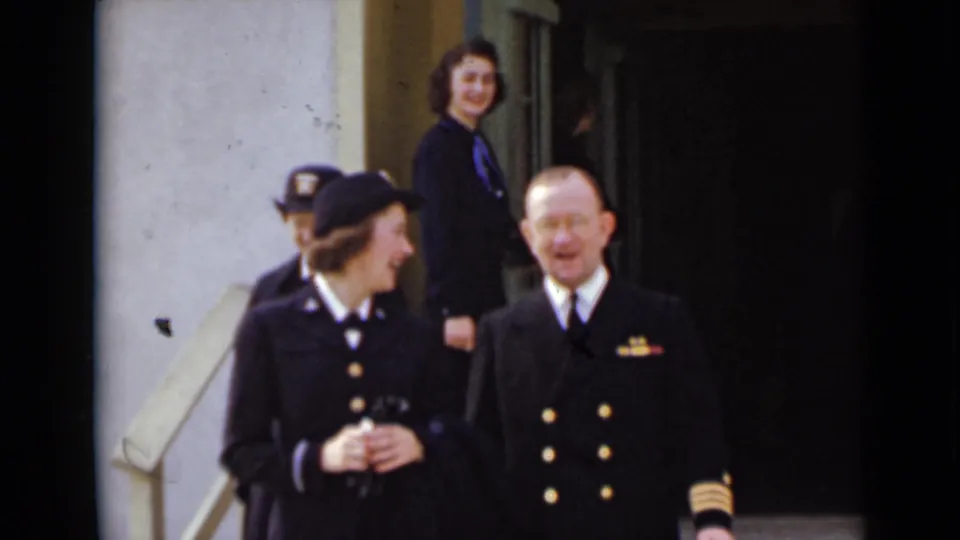 A woman in uniform holding a small object stands near a decorated male officer at the building entrance in the 1947 New York clip.