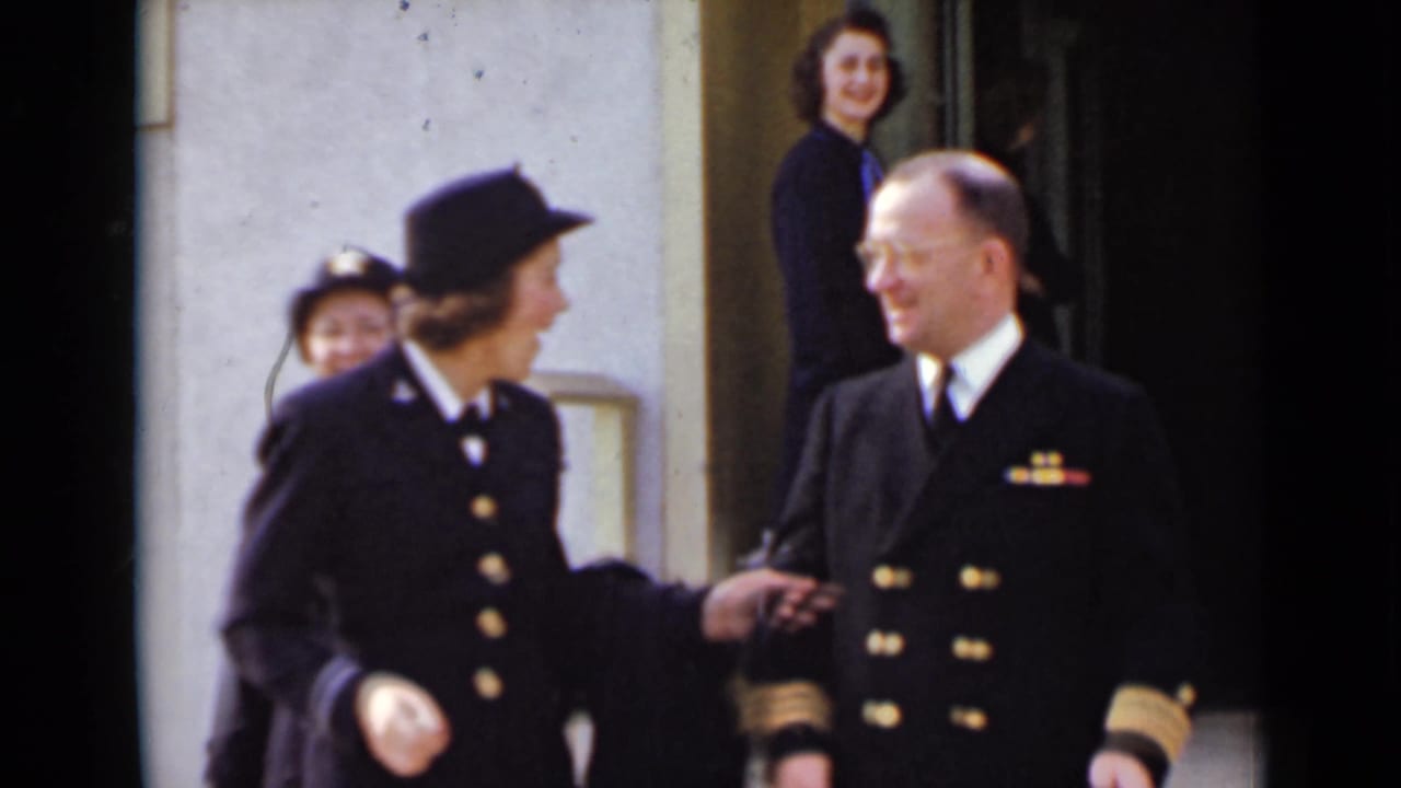 Uniformed man and woman smiling near a doorway as others stand behind them.