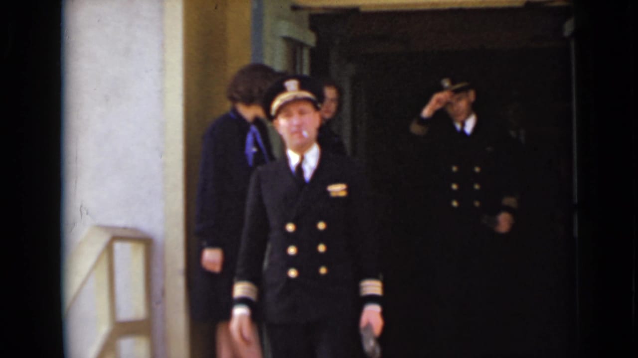 Uniformed woman walks out of a dark doorway while another uniformed man salutes behind her.