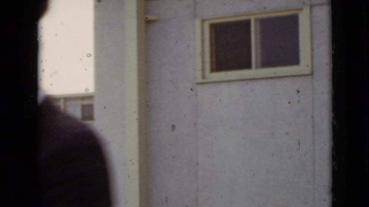 Partial view of a building wall and window with a blurred figure at the left edge.