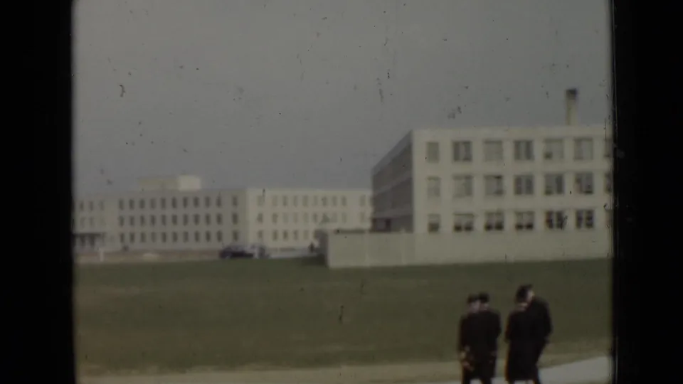 1947 New York frame with uniformed figures at the edge of a broad lawn and large institutional buildings in the background.