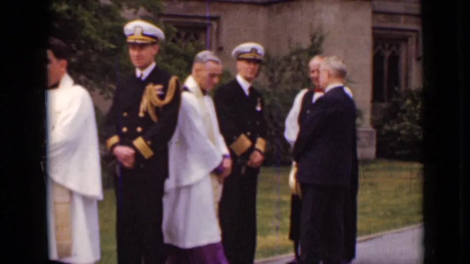 Uniformed officers, clergy in white vestments, and suited men gather near a church lawn in 1947 New York home-movie footage.