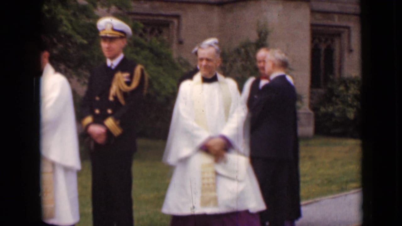 Naval officer and clergy stand outside a stone church with a suited man nearby.