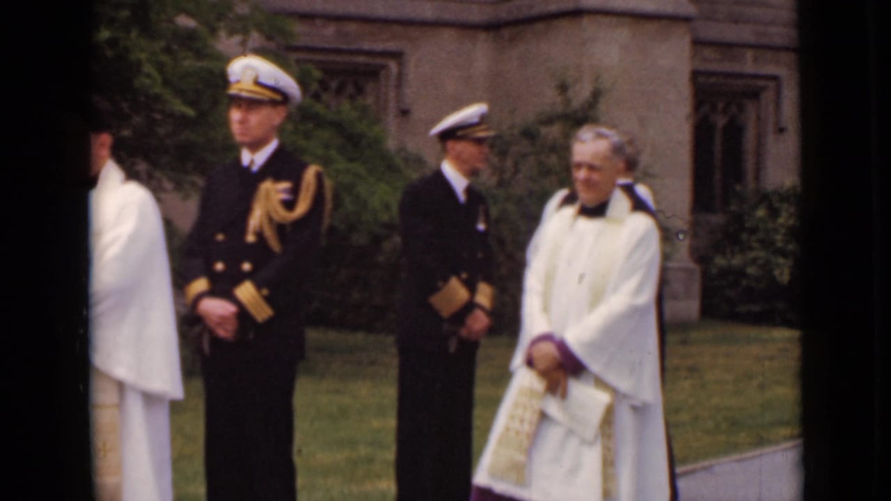 Two naval officers and clergy stand outside a church near lawn and shrubs.