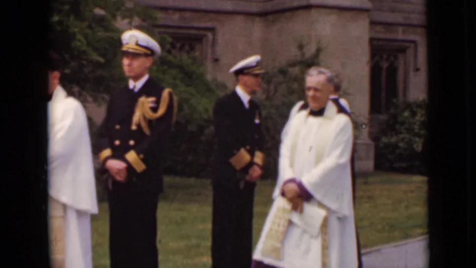 Two naval officers in dark dress uniforms stand with clergy in white vestments outside a New York stone church in 1947 footage.