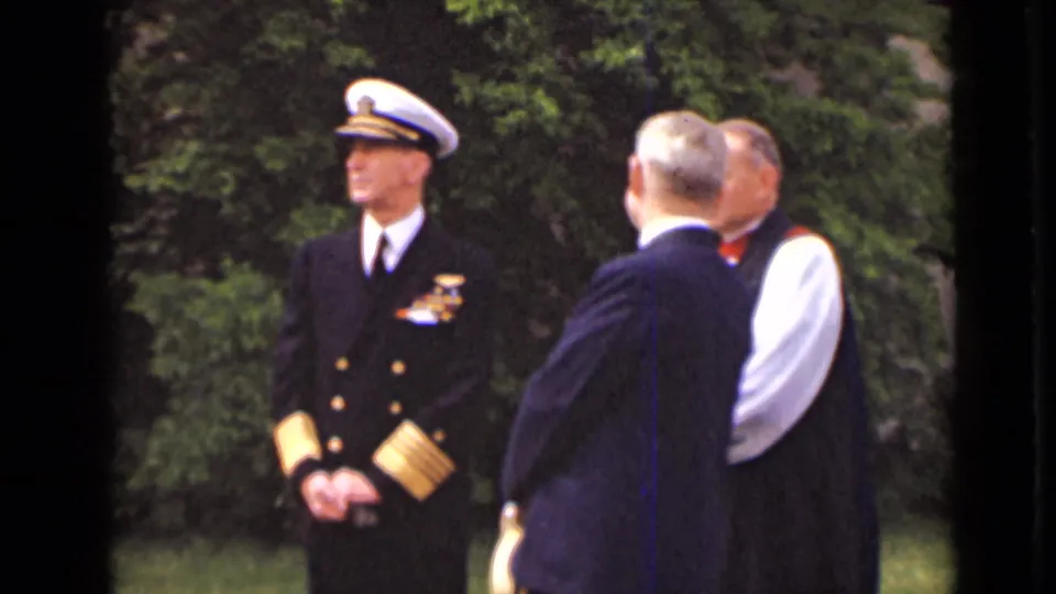 The naval officer remains at attention while two suited men turn toward him in 1947 New York outdoor home-movie footage.