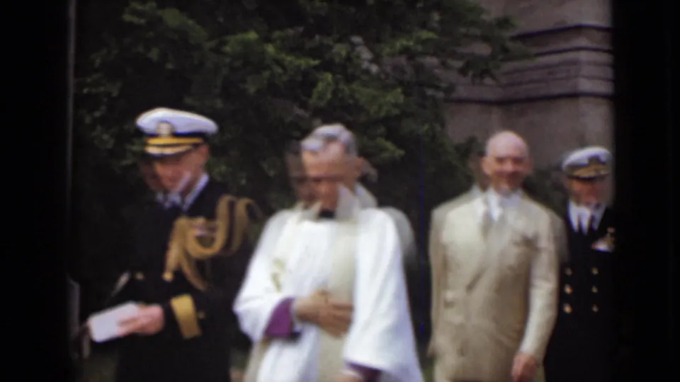 A clergyman in white and purple vestments walks with a naval officer and suited men in the 1947 New York outdoor gathering.