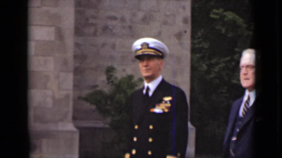 In metadata-supported 1947 New York, a naval officer in dress uniform stands beside a suited man near a stone building and trees.