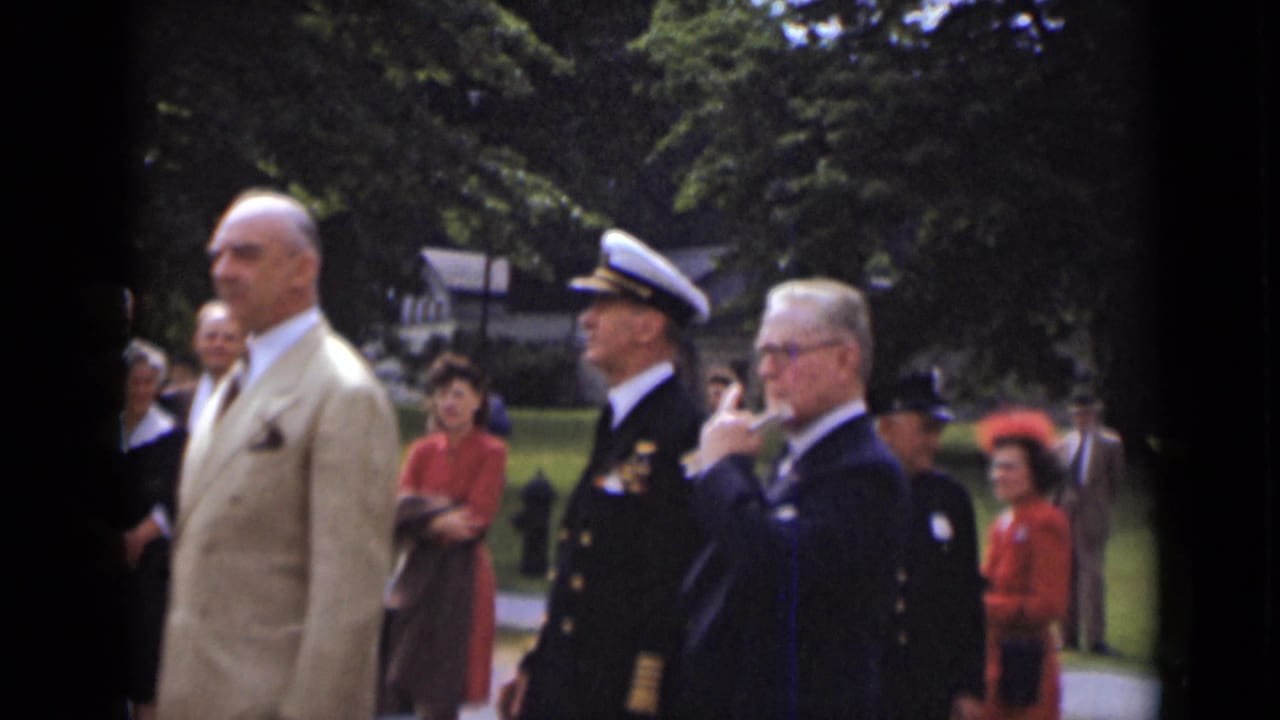 A formal outdoor crowd in New York, supported by metadata as 1947, includes a naval officer, suited men, and women in red dresses near trees and lawn.