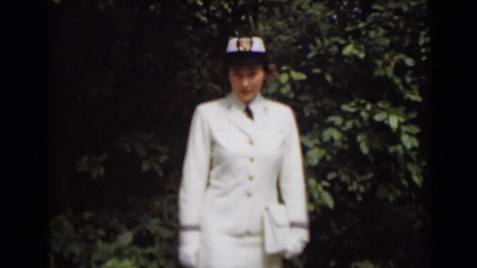 In 1947 New York footage, a woman in a white military-style uniform, gloves, tie, and cap stands before leafy greenery.