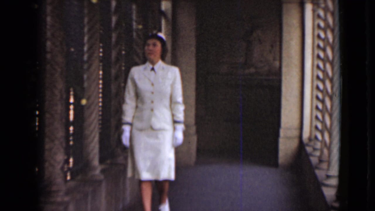 Woman in white standing or walking in an ornate stone hallway.