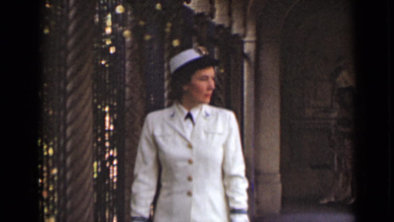 Uniformed woman in white jacket and cap looking to the side inside an ornate space.