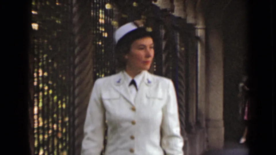 Closer 1947 New York frame of a uniformed woman in white gloves and cap walking past decorative columns.