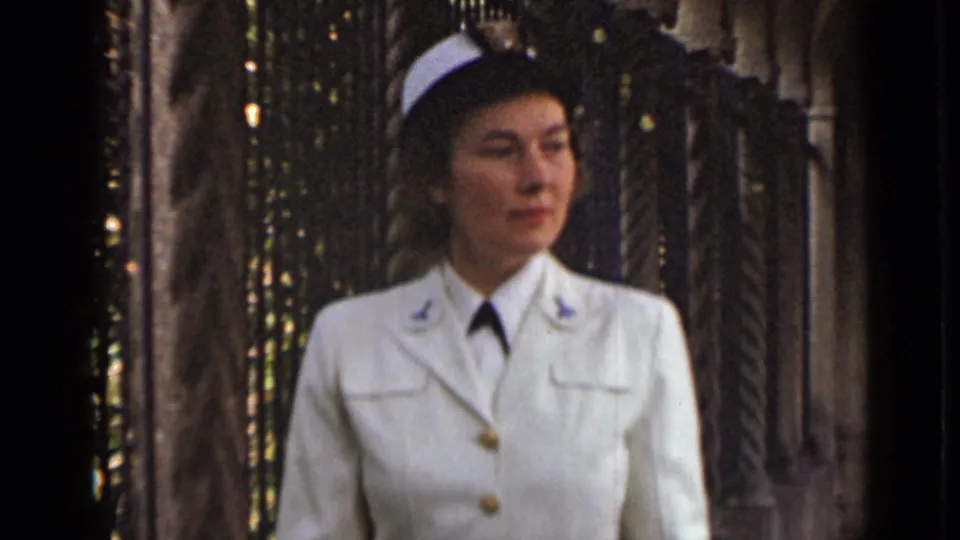 The 1947 New York home-movie frame shows a uniformed woman in white cap, gloves and jacket near ornate columns.
