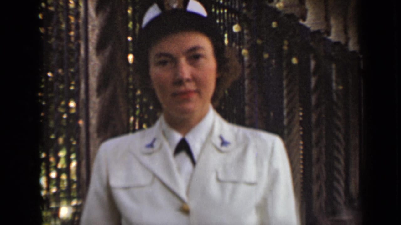 Woman in a white uniform and cap facing the camera near dark ironwork.