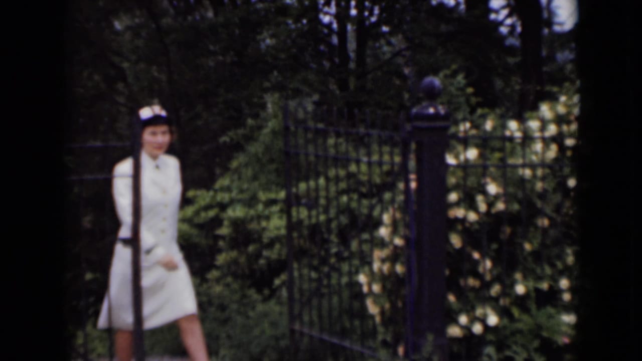 Woman in white uniform stands near a black iron garden gate.