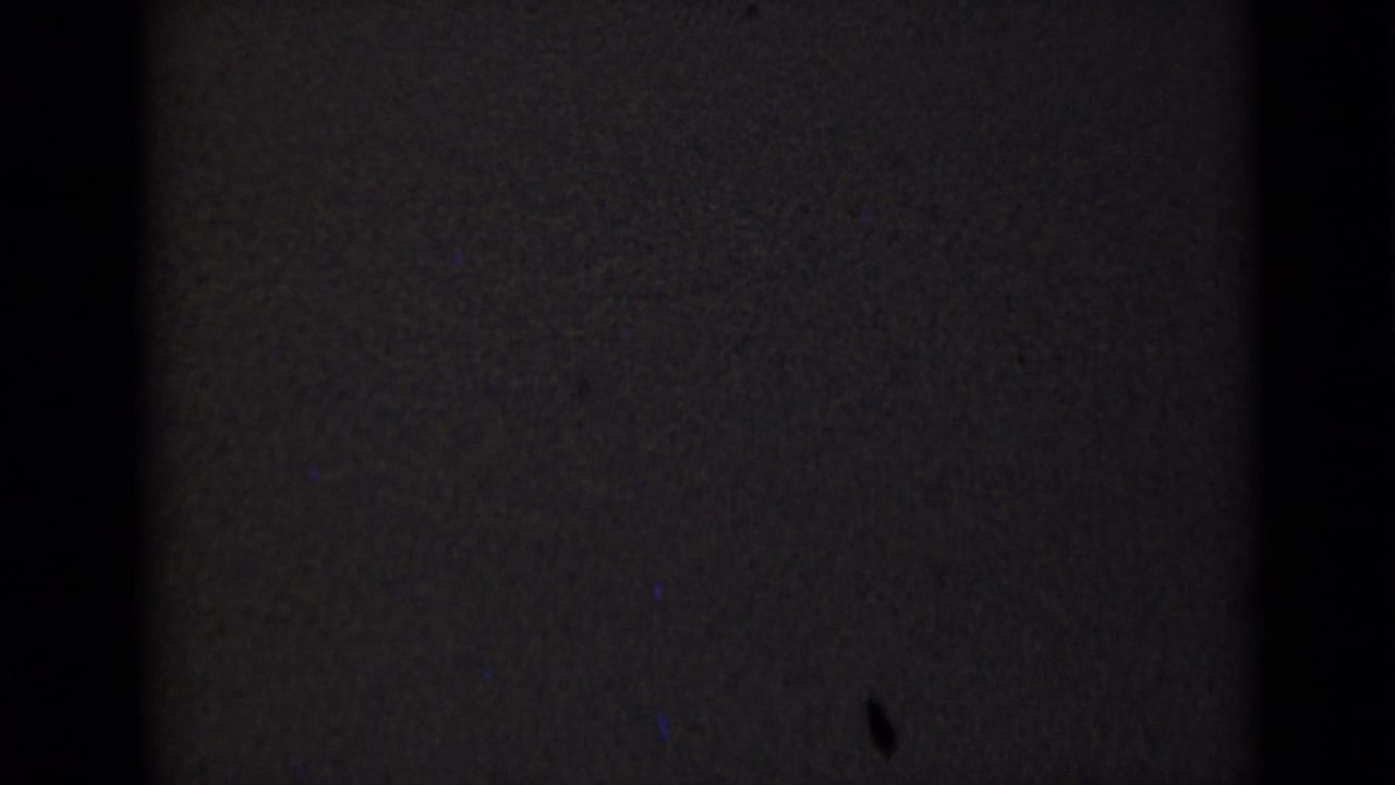 A dark transitional 8mm frame with only faint film texture visible and no clear subject detail.