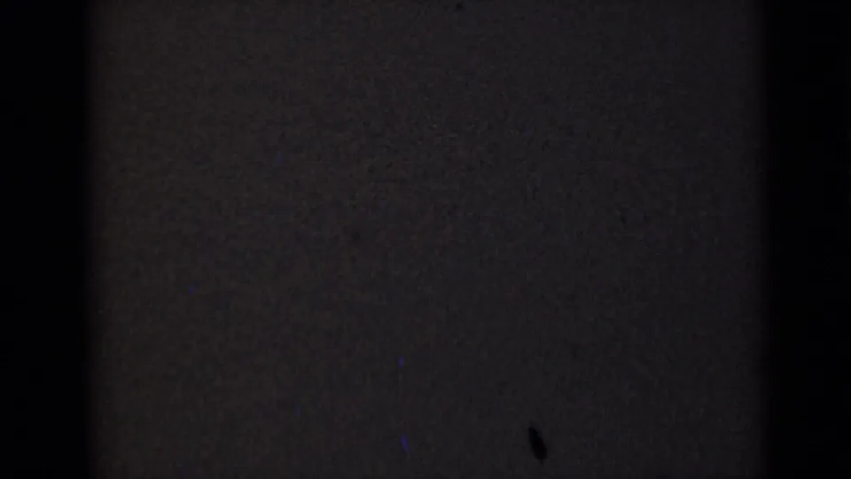 A dark transitional 8mm frame with only faint film texture visible and no clear subject detail.