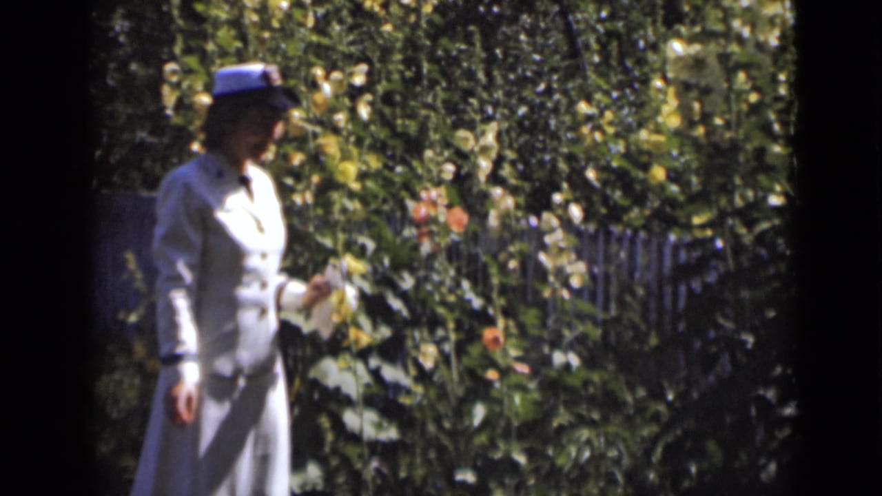 Woman holding a small pale object while standing near flowering plants.