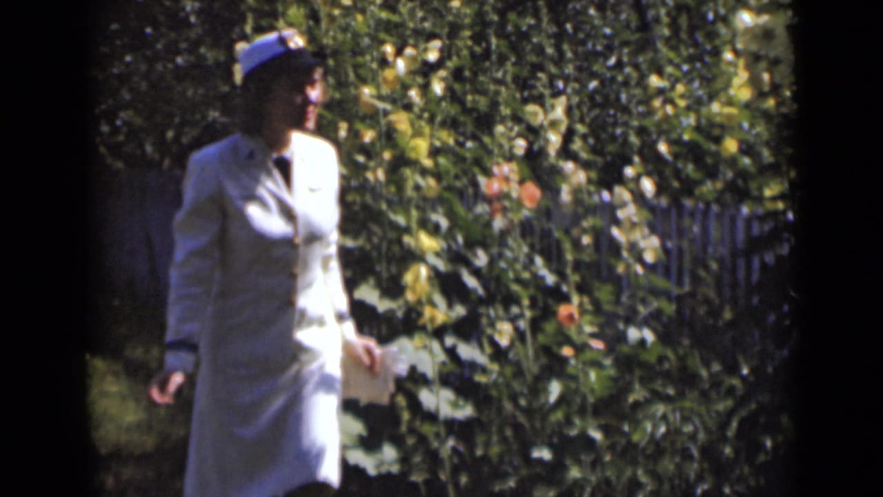 Woman in a light outfit walks beside dense flowering plants.