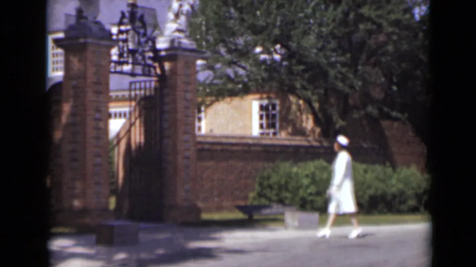 The woman walks rightward past the brick entrance, greenery, and partial historic building details in 1947 New York footage.