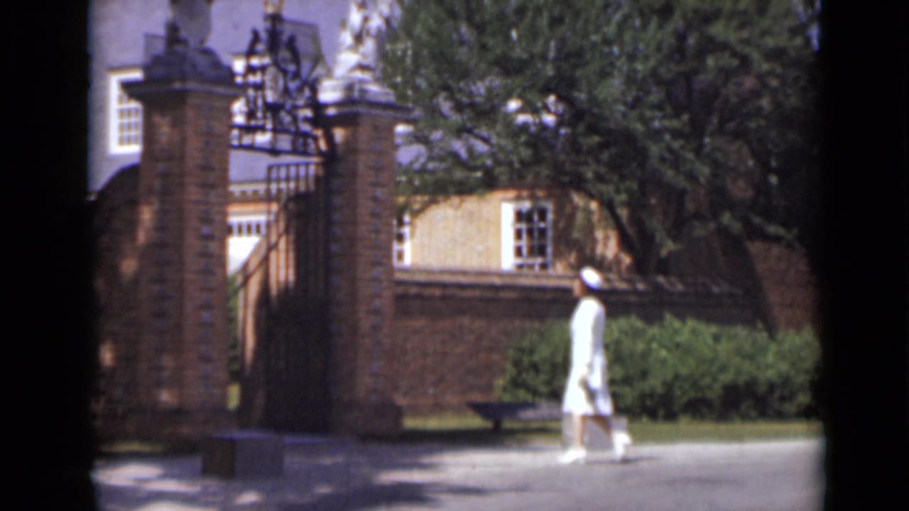 Woman in a white dress walks across a courtyard toward a brick gate.
