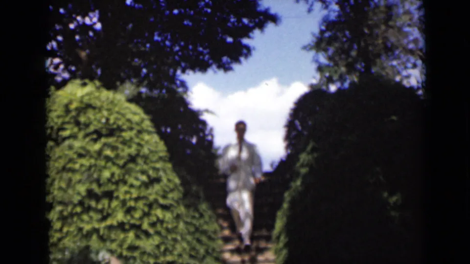 A soft-focus 8mm frame shows the suited man closer to camera while descending the hedge-lined garden stairs in New York, 1947.