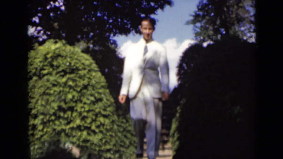 The man smiles as he nears the camera in a white suit, descending from a hedge-lined garden stairway in 1947 New York footage.