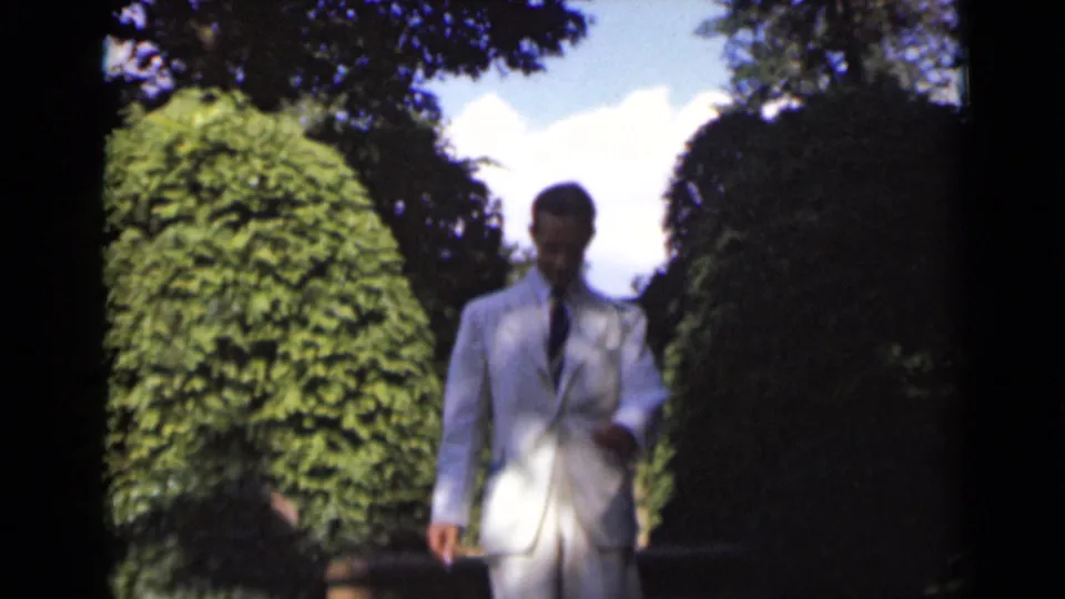 The man in a white suit walks slowly down a shrub-lined stairway in the 1947 New York home-movie scene.